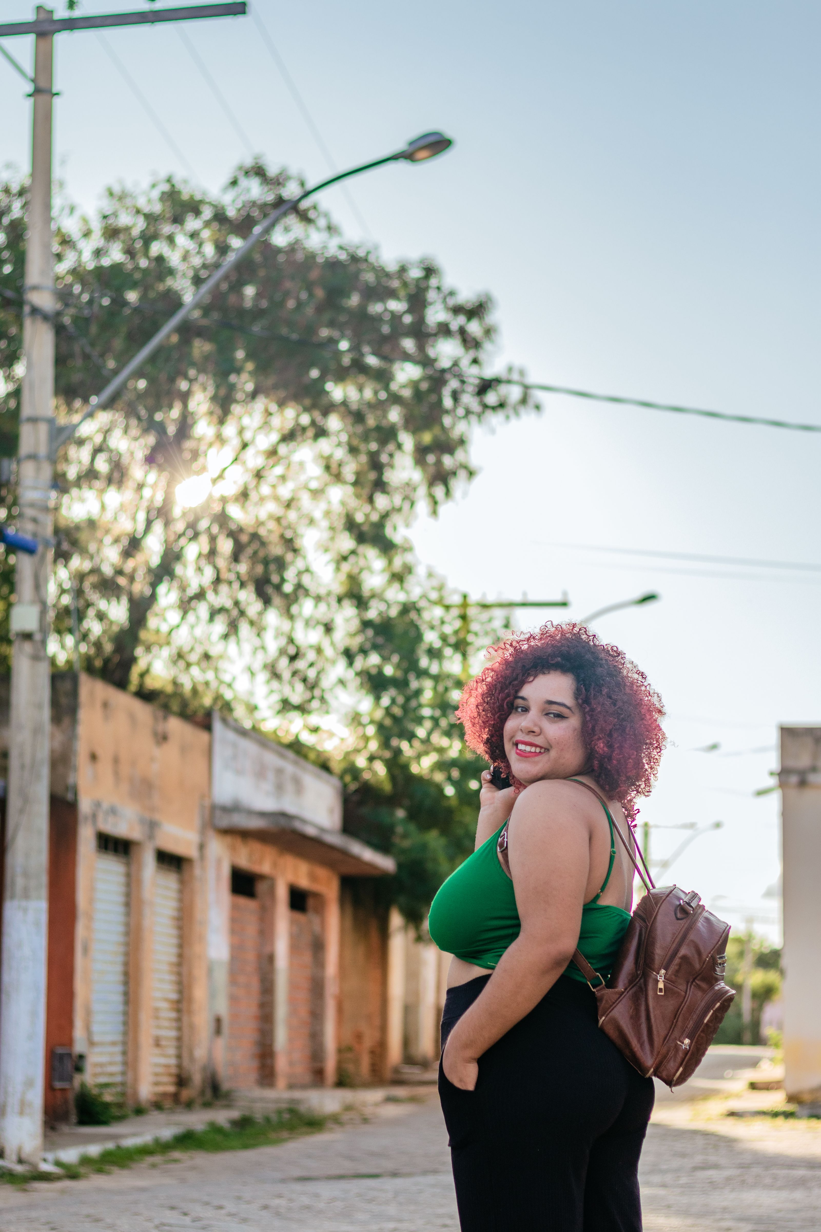 Uma mulher plus size com cabelo vermelho sorri confiantemente enquanto caminha por uma rua da cidade, demonstrando estilo e autoconfiança.