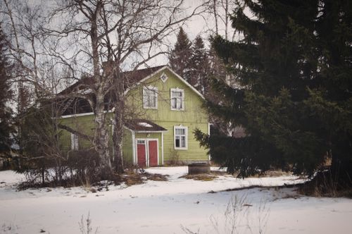 Free Charming green cottage surrounded by snow and bare trees in a peaceful winter setting. Stock Photo