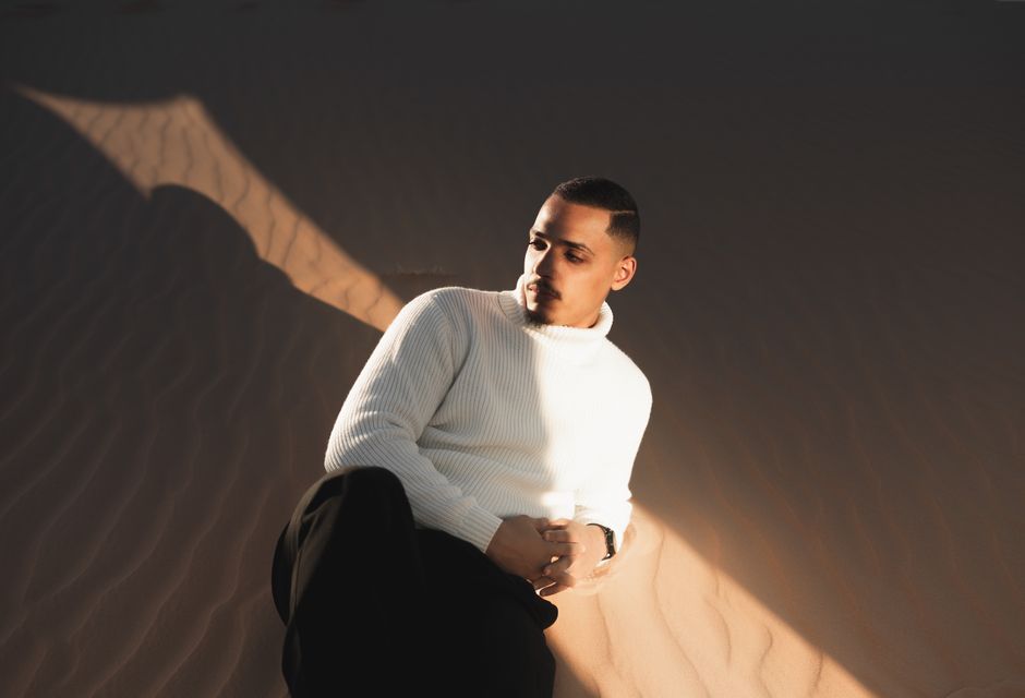 A man dressed in a white turtleneck rests on the sand in Ouargla, Algeria.