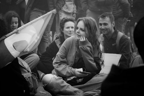 Free Group of young adults sitting together during an outdoor event with a flag noticeable in a black and white setting. Stock Photo