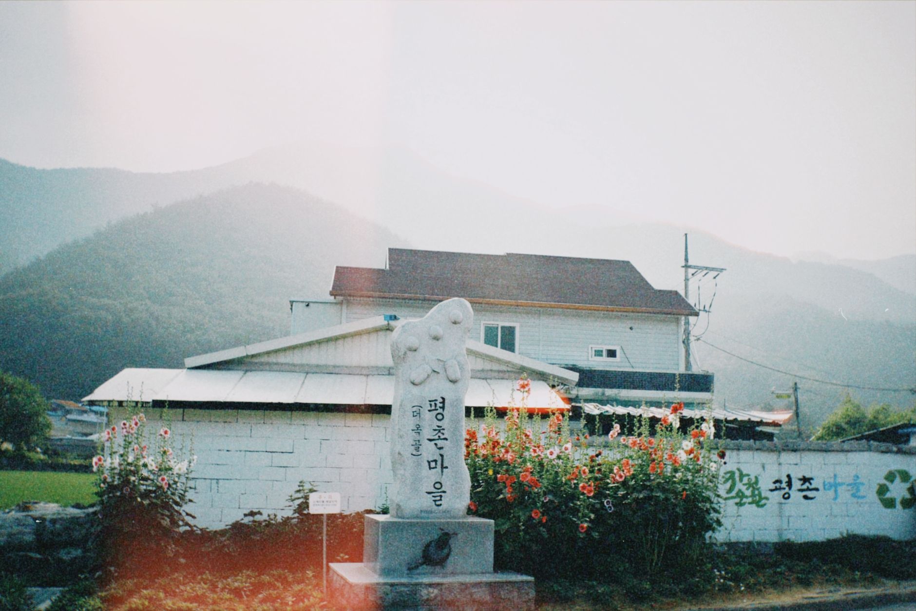 Tranquil South Korean village scene with a mountain backdrop and local monument.