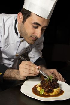 Mid adult chef skillfully garnishing meat dish with precision on a plate in studio setting.