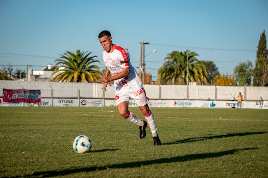 A soccer player in sportswear dribbles the ball on an outdoor field during a daytime match.