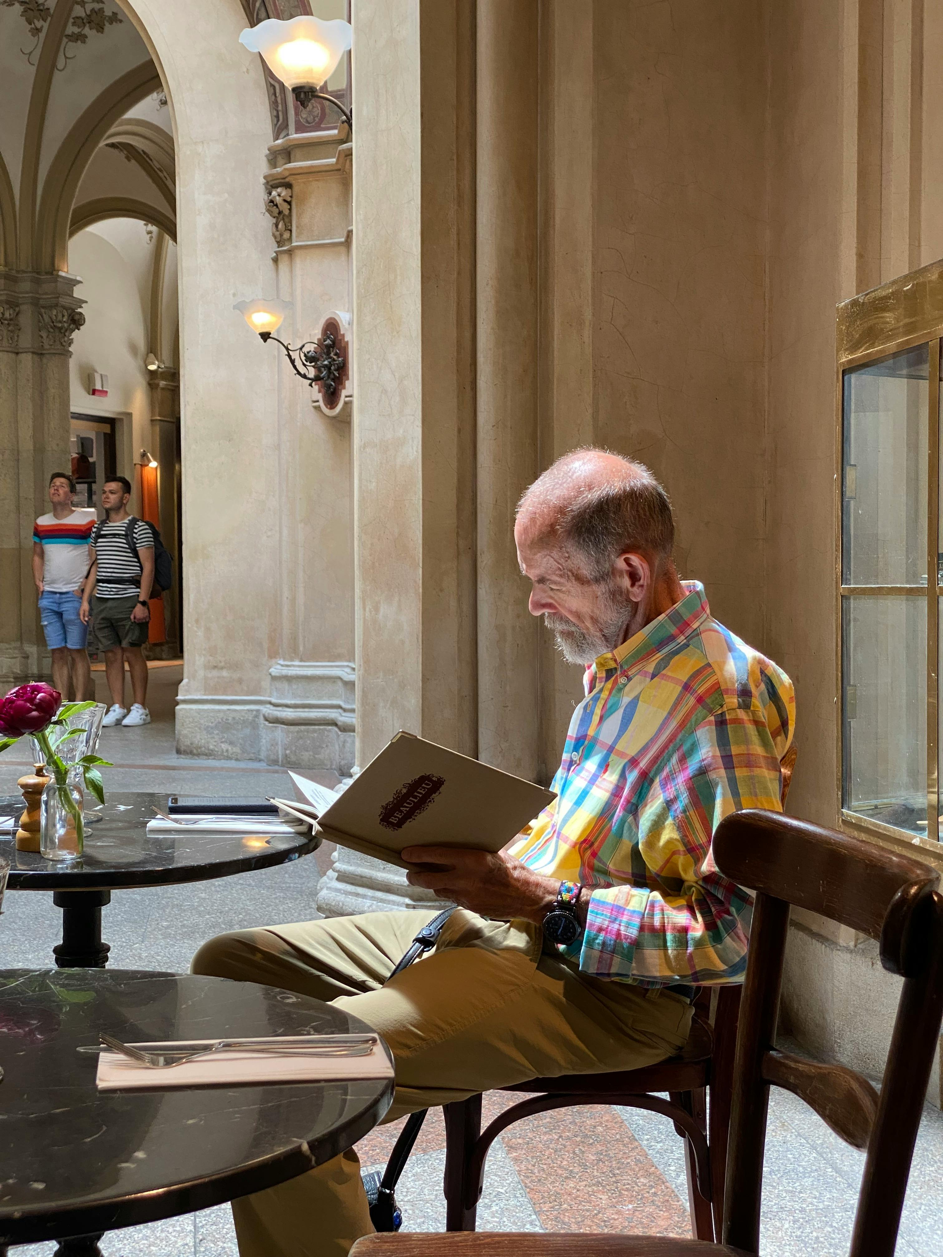 Senior man reading a menu in a stylish Vienna cafe with elegant architecture.