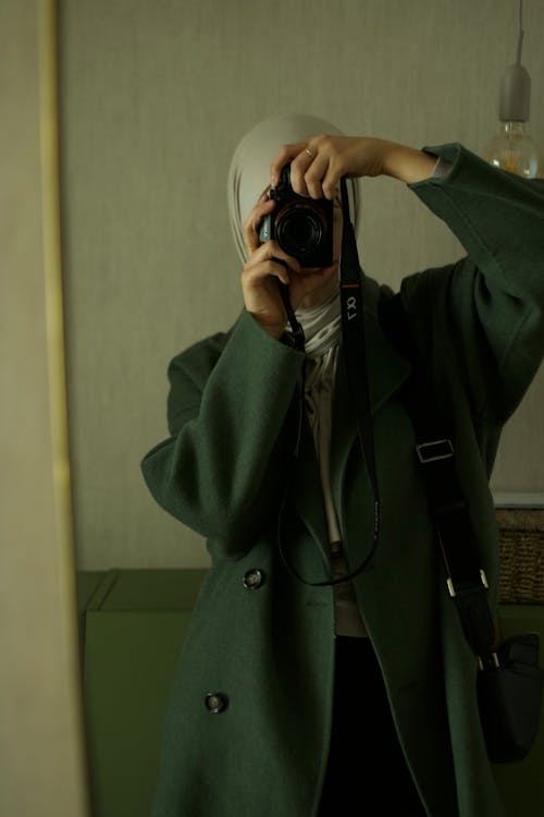 Woman in Coat Taking Pictures in Mirror