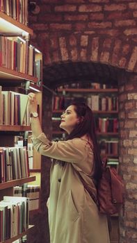 A young woman browsing books in a brick-lined library, exuding a warm and cozy atmosphere.
