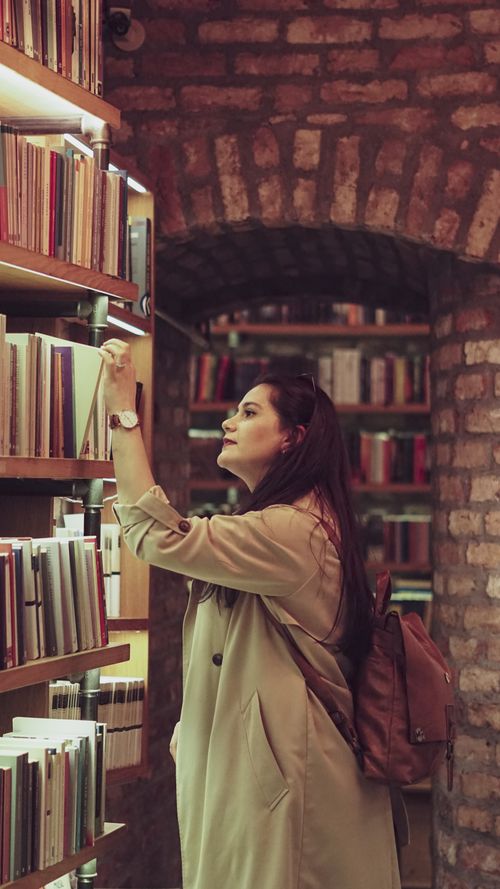 Free A young woman browsing books in a brick-lined library, exuding a warm and cozy atmosphere. Stock Photo