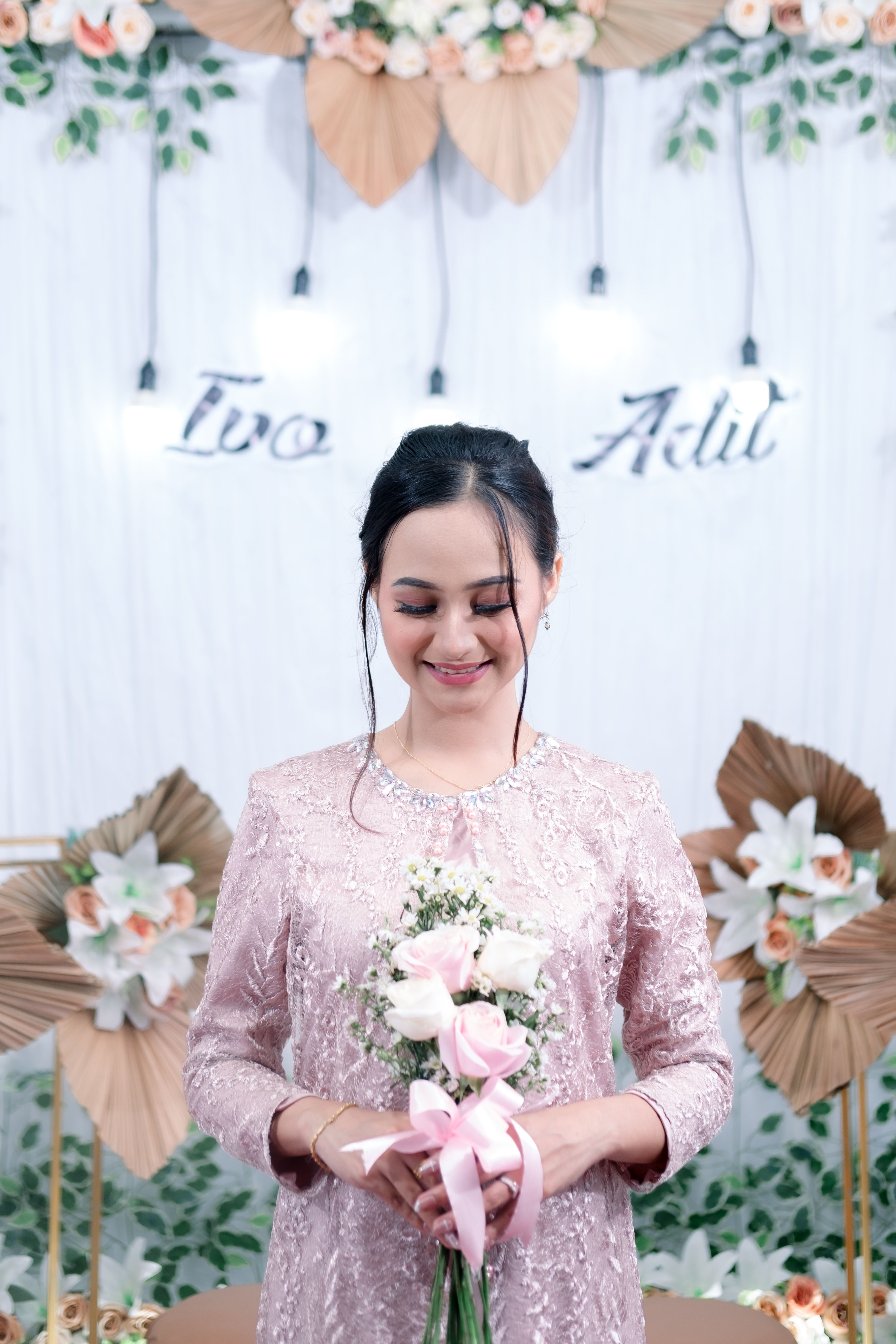 A smiling bride holds a bouquet in a charming Indonesian wedding setting.