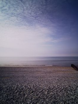 Tranquil rocky beach in Pensarn, Wales, with calm sea and cloudy sky.