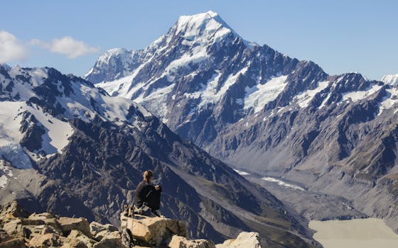 A hiker resting while overlooking the majestic Mount Cook in New Zealand's Southern Alps.