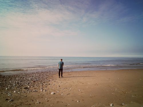 Free A solitary figure walks along the serene Pensarn Beach, Wales, enjoying nature's tranquility. Stock Photo