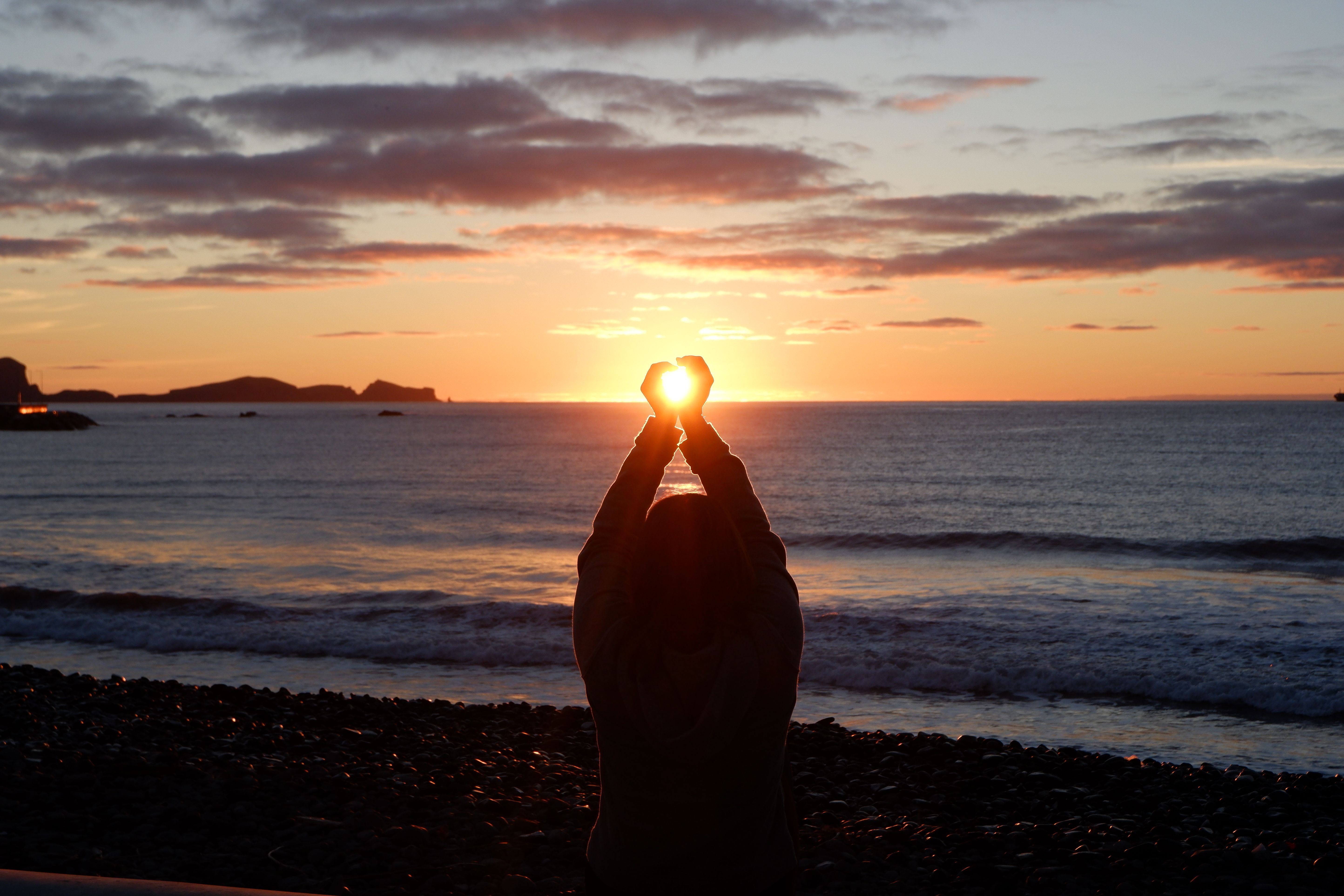 Back View of Woman Sitting with Arms Raised on Sea Shore at Sunset ...