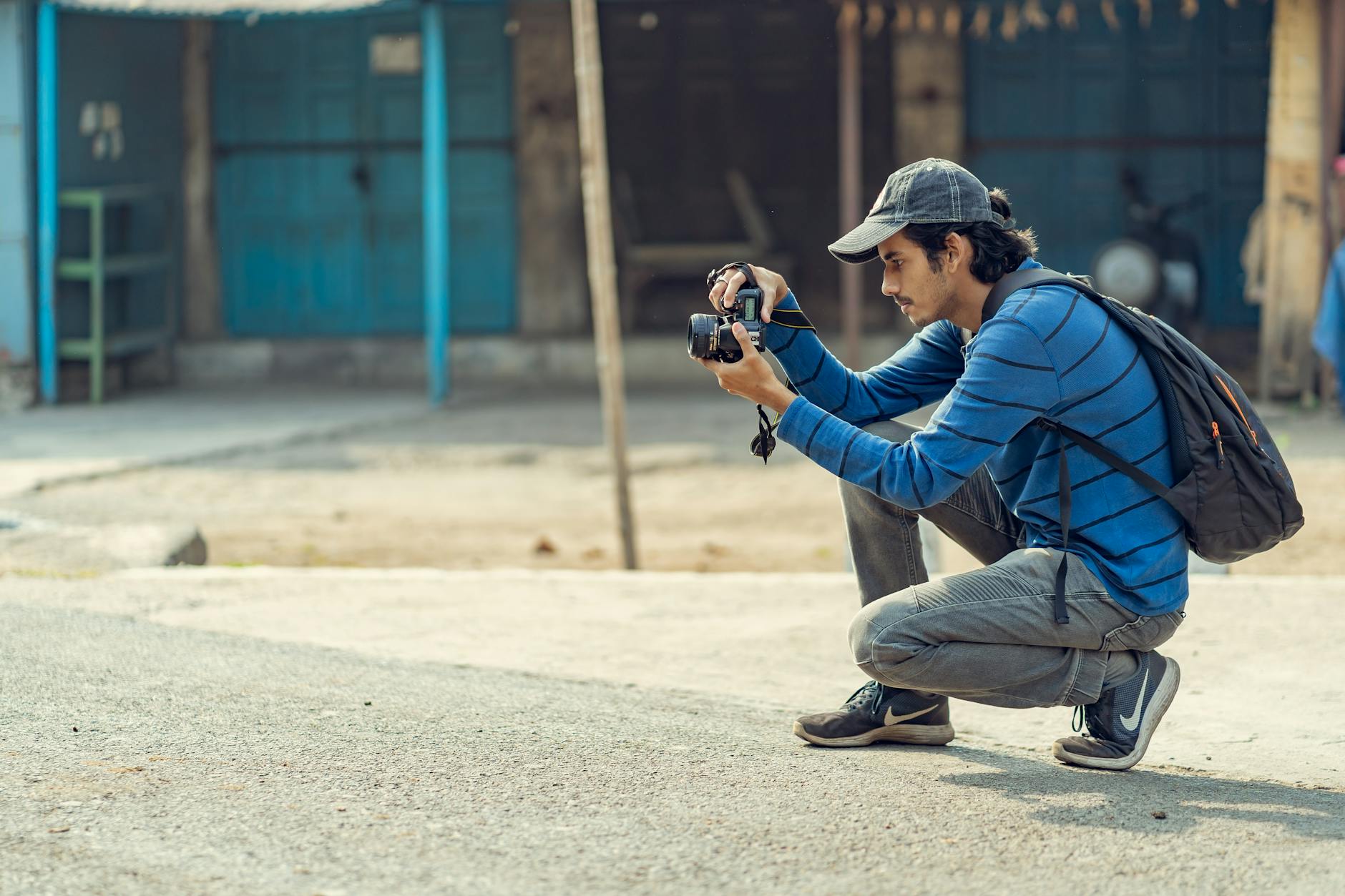 A young man crouching to take photos with his DSLR camera in an urban environment.