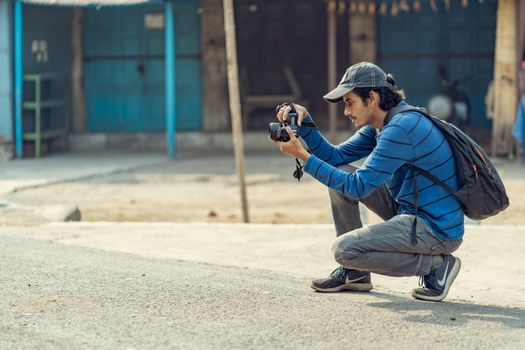 A young man crouching to take photos with his DSLR camera in an urban environment.