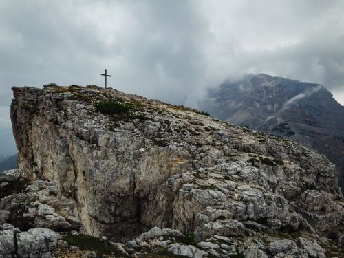 Free A striking view of a rocky peak with a cross, surrounded by dramatic clouds in Dolomites, Italy. Stock Photo