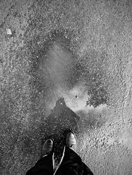 Shoes standing on wet pavement with a puddle reflecting a silhouette.