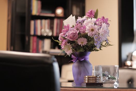 A beautiful bouquet of flowers in a purple vase adorns an office with bookshelves.