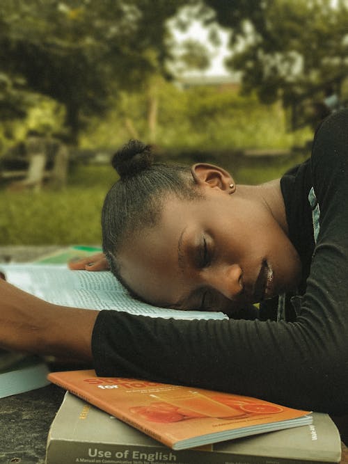 Free Young Woman Lying with Her Head on the Books in a Park  Stock Photo