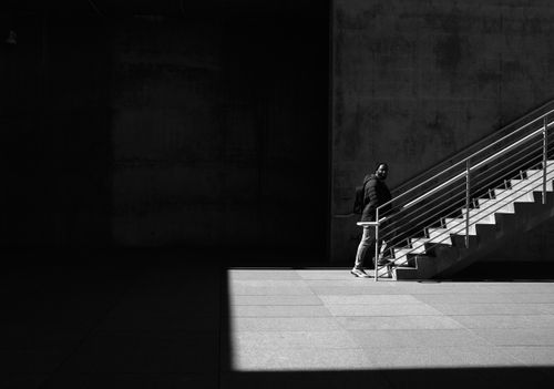 Free A man walks up outdoor stairs in a modern urban setting, captured in black and white. Stock Photo