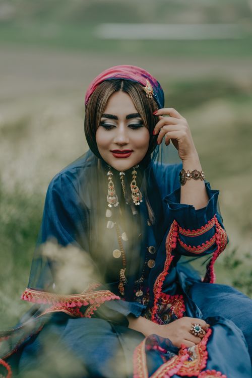 Free A beautiful woman in traditional blue dress and headscarf, sitting outdoors with natural background. Stock Photo