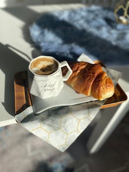 Elegant breakfast setting with a coffee mug and croissant on a tray, perfect for a relaxed morning.