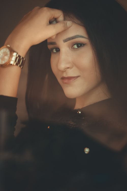 Free A close-up portrait of a brunette woman smiling with her hand on her forehead, wearing a wristwatch. Stock Photo