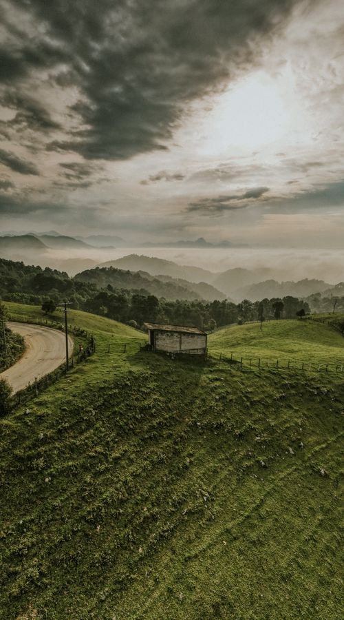 Free Captivating rural landscape featuring hills, a hut, and a winding road. Stock Photo