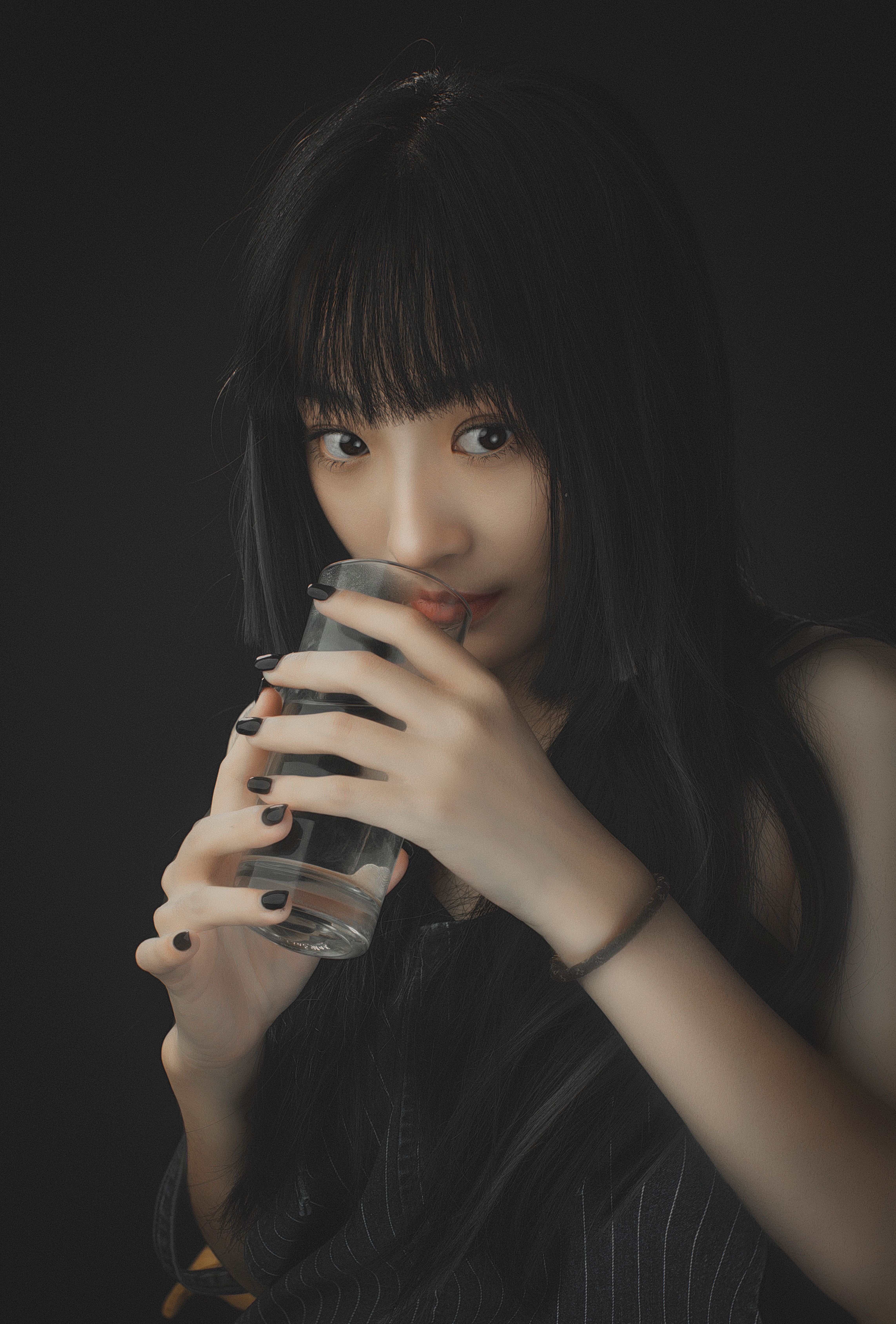 Moody portrait of a young woman with long hair holding a glass in a studio setting.