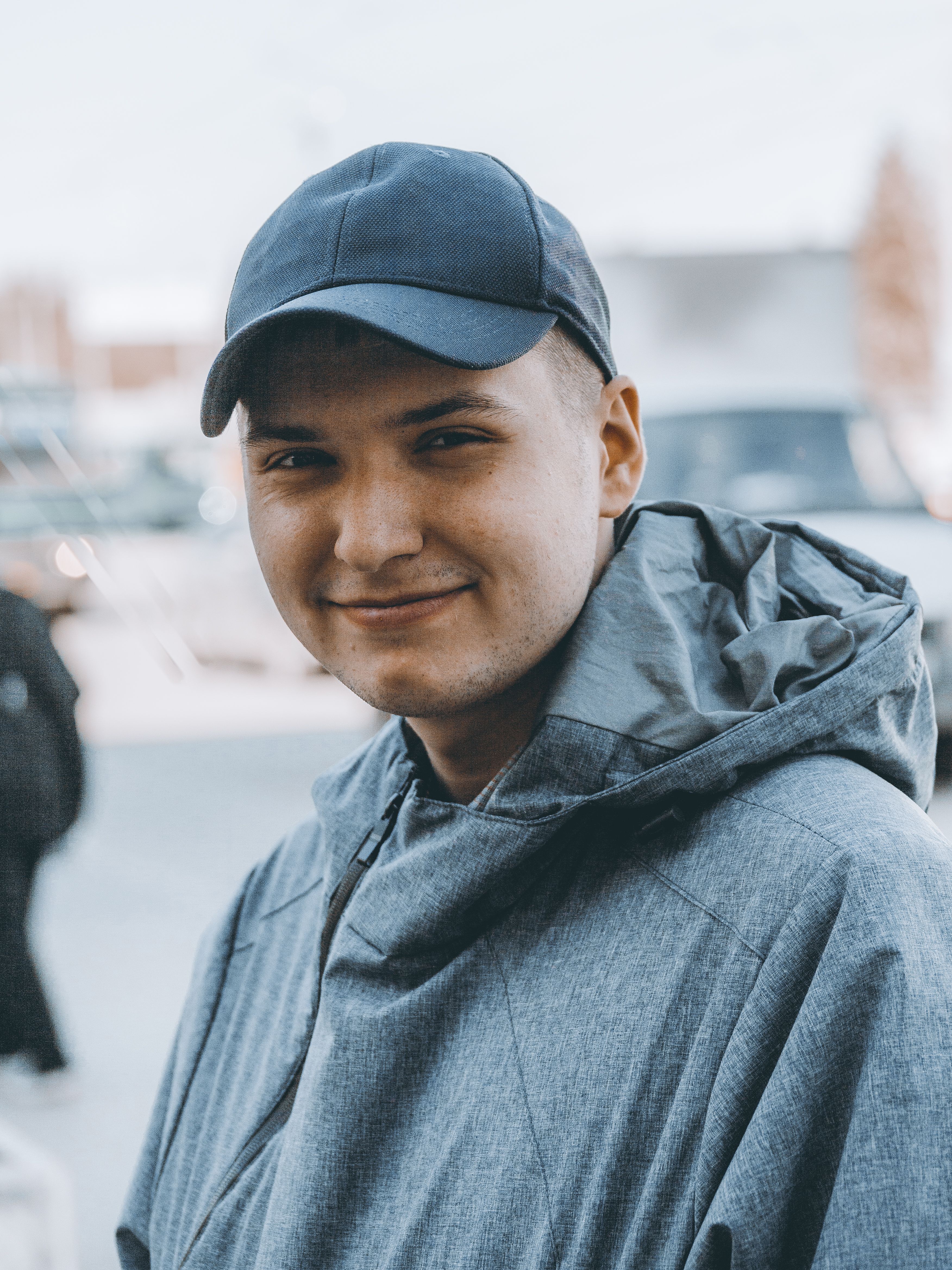 Smiling young man in a cap and jacket outdoors on city street.