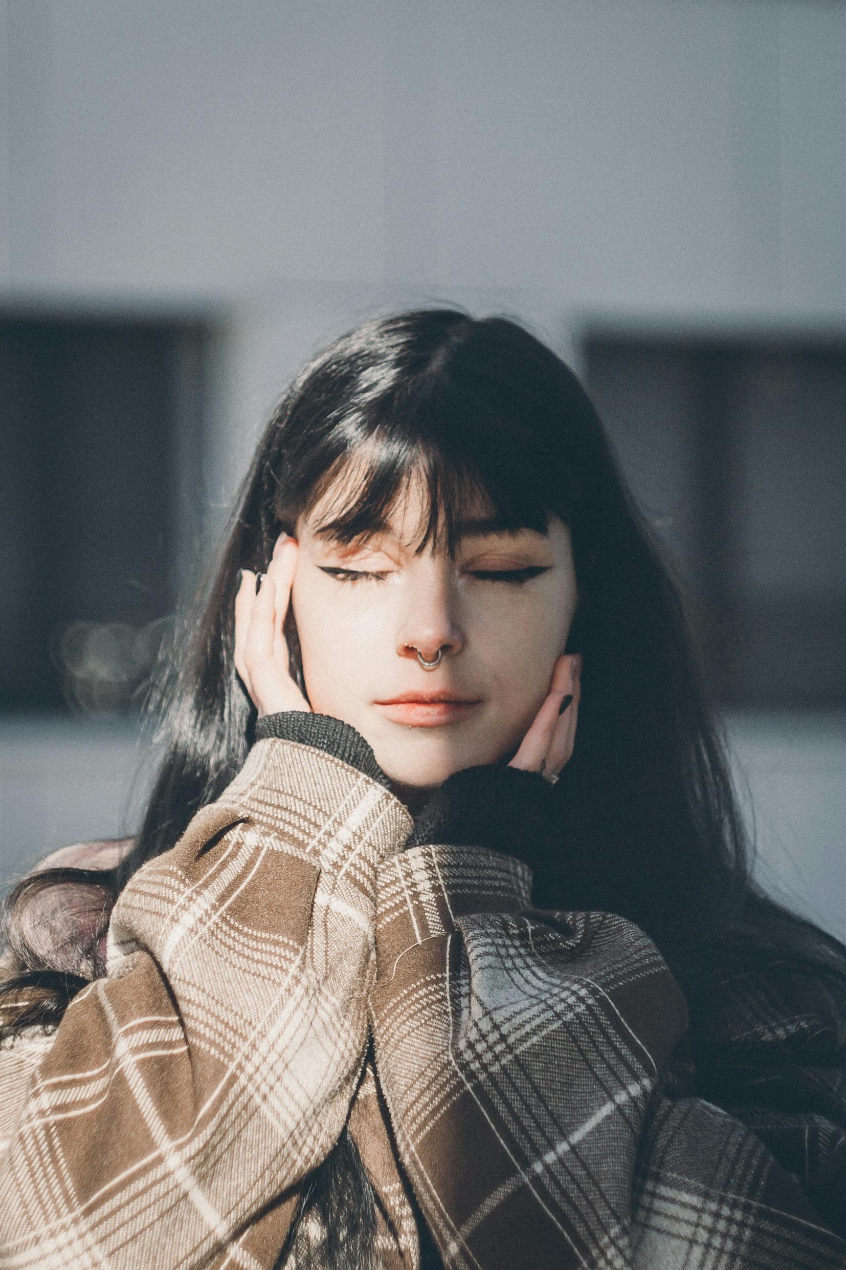 Serene portrait of a woman with black hair and a nose ring, basking in sunlight.