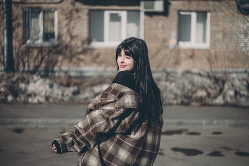 Young Woman in a Checkered Jacket Standing Outdoors in City 