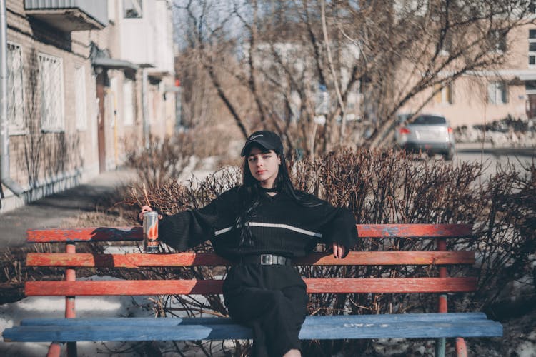 Woman Sitting On Bench With Can Of Soda In Hand