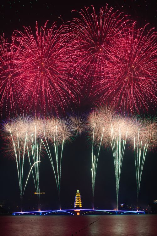 Free Dazzling fireworks explode over a brightly lit waterfront at night. Stock Photo