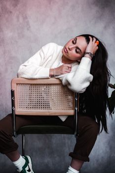 Portrait of a woman with long brunette hair posing stylishly on a chair indoors.