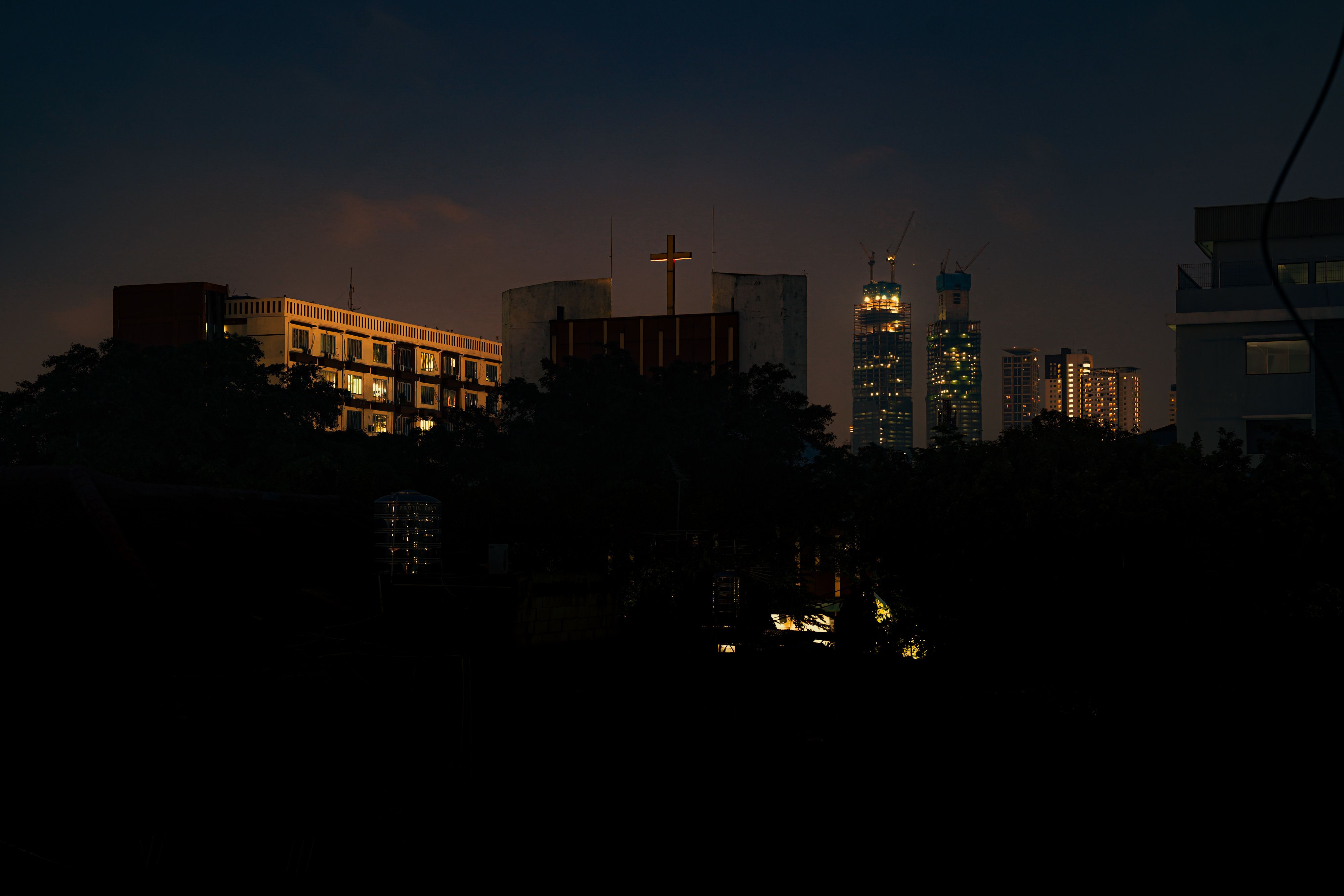 Night view of Jakarta skyline with a brightly lit cross in the foreground.