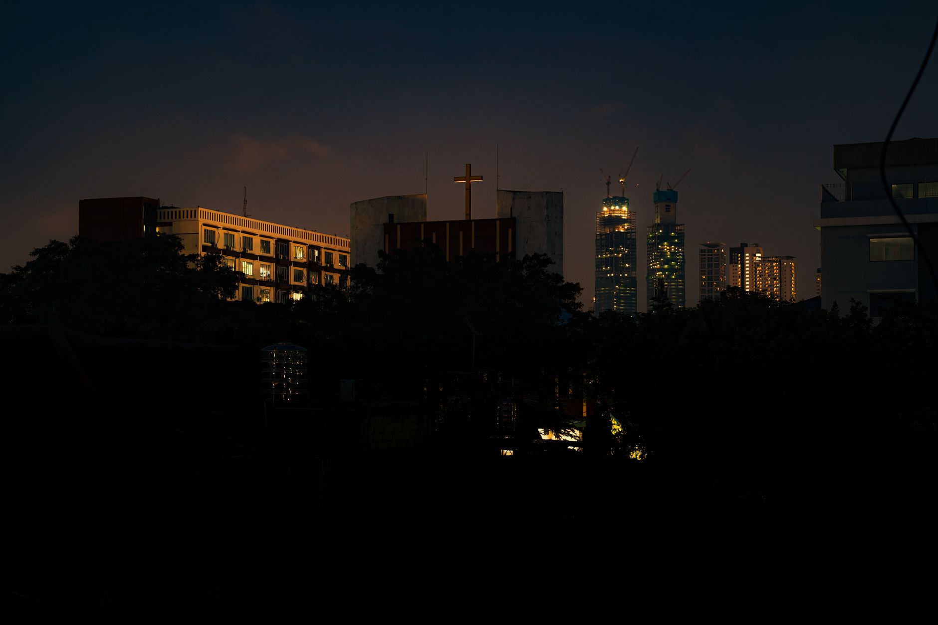 Night view of Jakarta skyline with a brightly lit cross in the foreground.