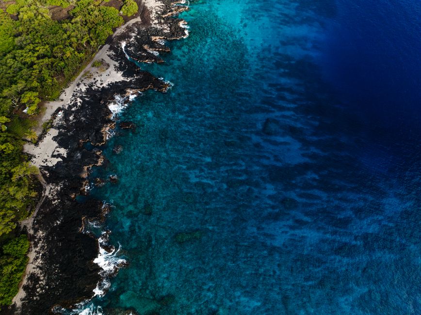 Stunning aerial view of the coastline in Honaunau-Napoopoo, Hawaii, showcasing vibrant blue waters and lush greenery.