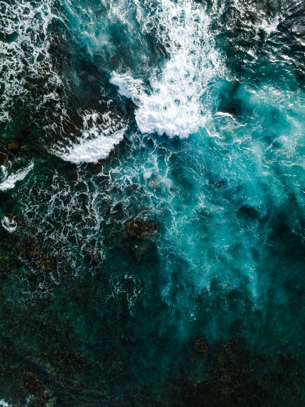 Photo by Josh Withers Captivating aerial shot of turquoise sea waves crashing on the rocky Hawaiian shore in vibrant sunlight.