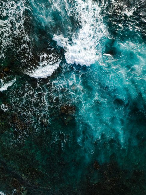 Photo by Josh Withers Captivating aerial shot of turquoise sea waves crashing on the rocky Hawaiian shore in vibrant sunlight.