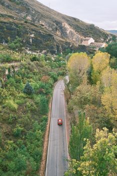 Aerial shot of a red car on a winding road through lush forests in Cuenca, Spain.
