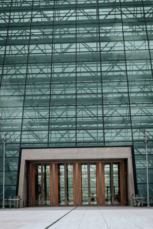 Free Striking modern glass facade with a wooden door entrance in an urban setting. Ideal for travel and architecture themes. Stock Photo