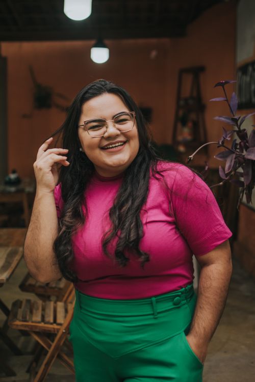 Free Happy woman with eyeglasses and long hair wearing a pink top, smiling indoors. Stock Photo