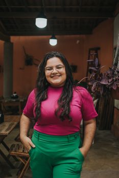 Smiling woman standing indoors wearing a vibrant pink and green outfit, exuding confidence and joy.