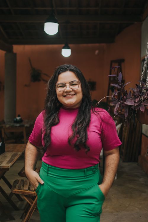 Free Smiling woman standing indoors wearing a vibrant pink and green outfit, exuding confidence and joy. Stock Photo