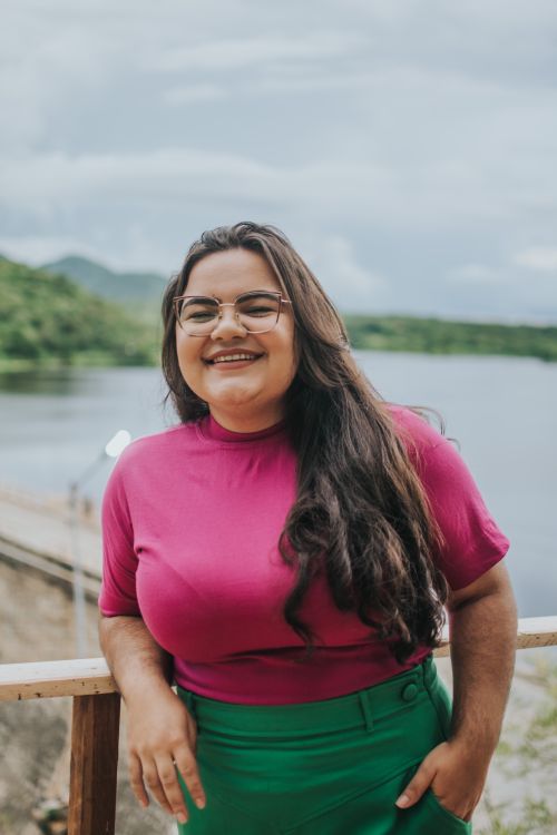 Free Happy woman with long hair and eyeglasses smiling by a scenic lake on a clear day. Stock Photo