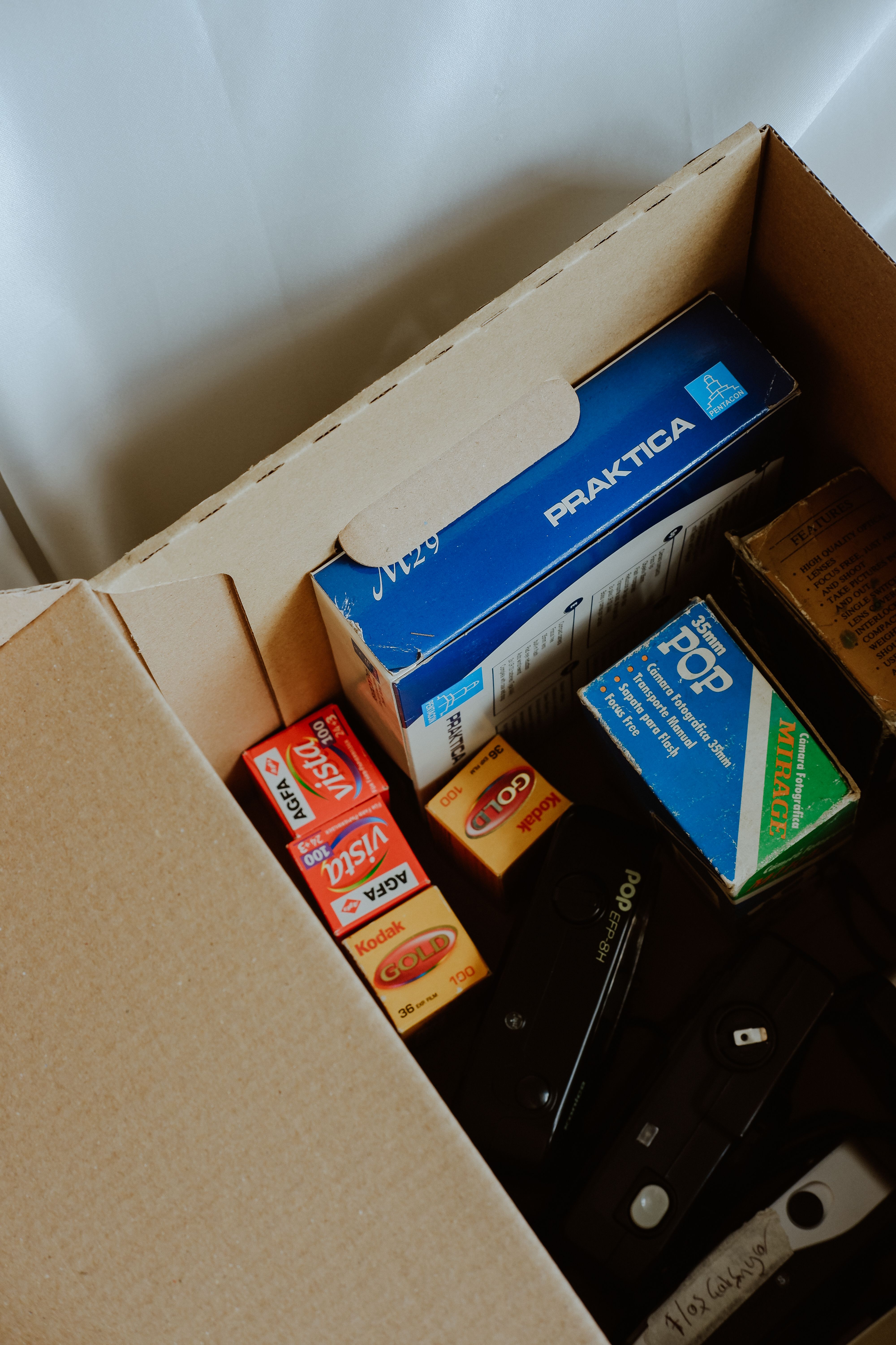 A collection of vintage photographic films and camera equipment stored in a cardboard box.
