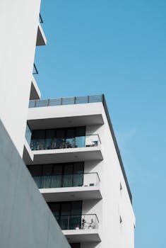 Modern white apartment building with balconies against a clear blue sky, showcasing minimalist design.