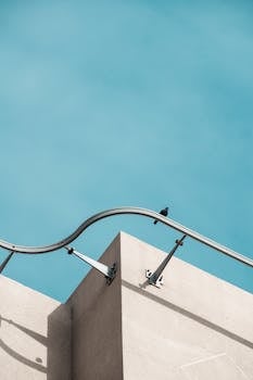 Minimalist architecture featuring a building corner with a bird perched on railing against a vivid blue sky.