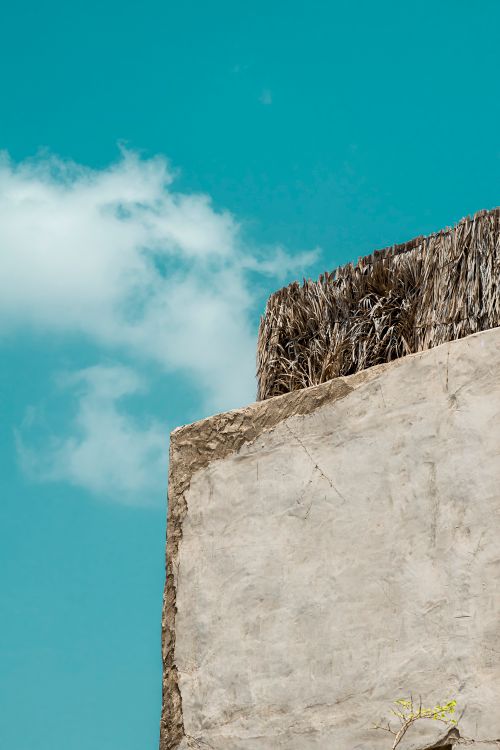 Free A textured wall with straw roofing under a blue sky, capturing minimalist architecture. Stock Photo