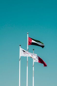 Three flags, including UAE, waving under a clear blue sky, symbolizing unity and patriotism.